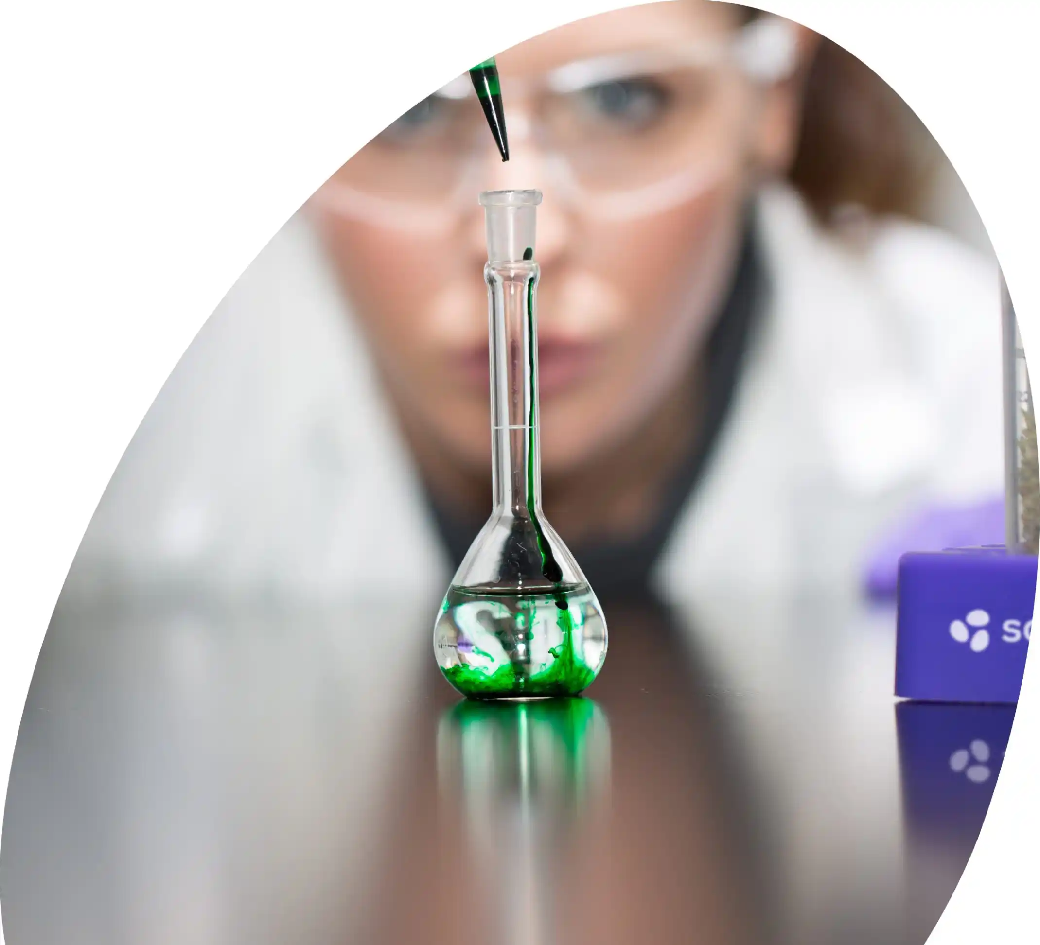 Female scientist adding green drops into a beaker